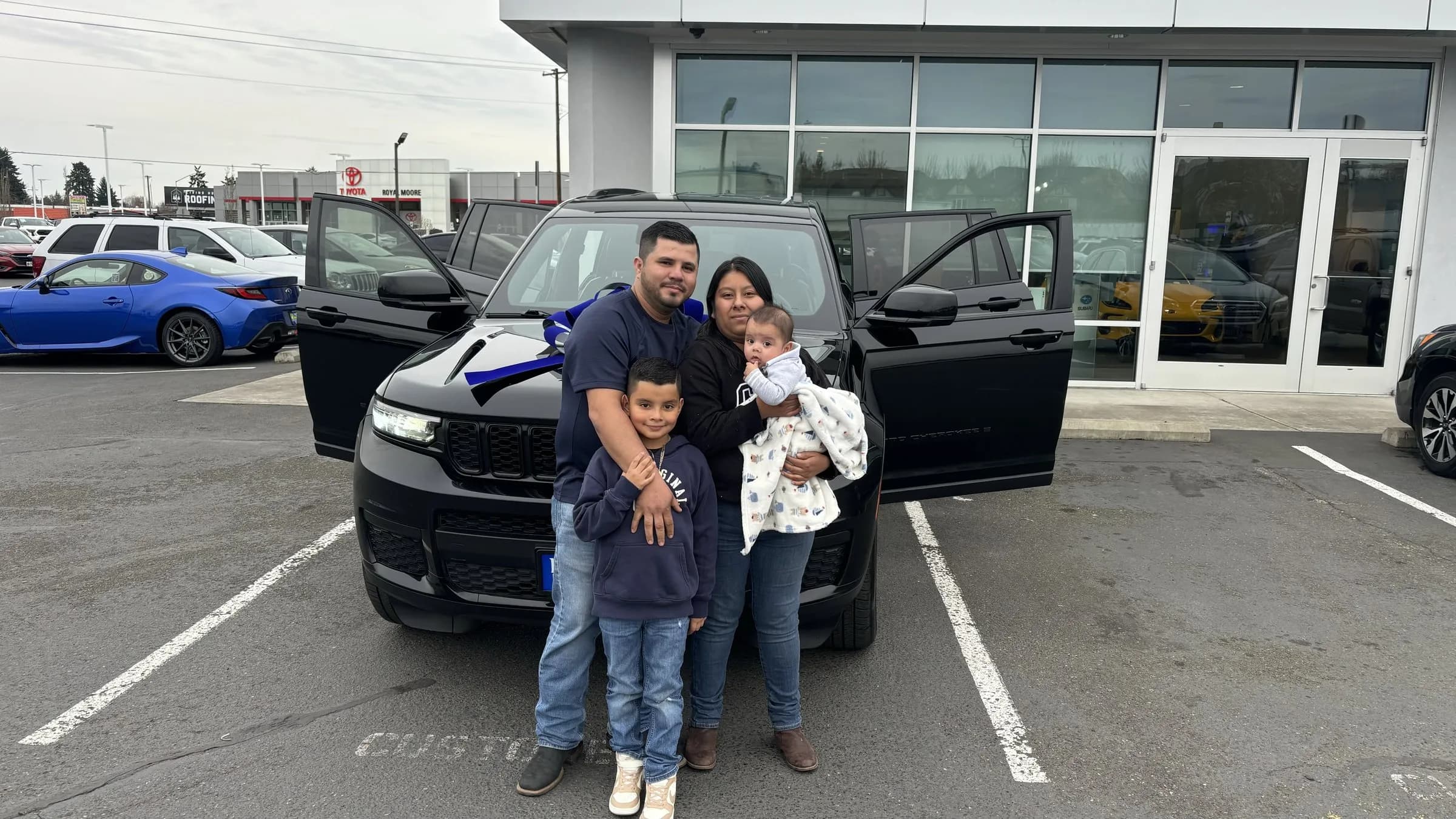 Family celebrating a Jeep delivery on the lot with a blue bow