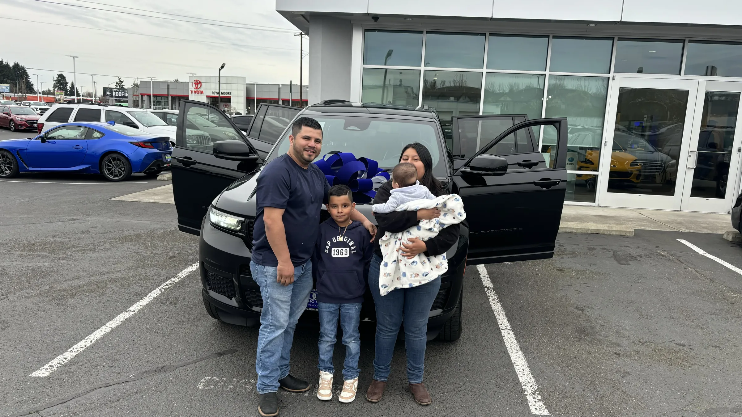 Family celebrating a Jeep delivery on the lot with a blue bow