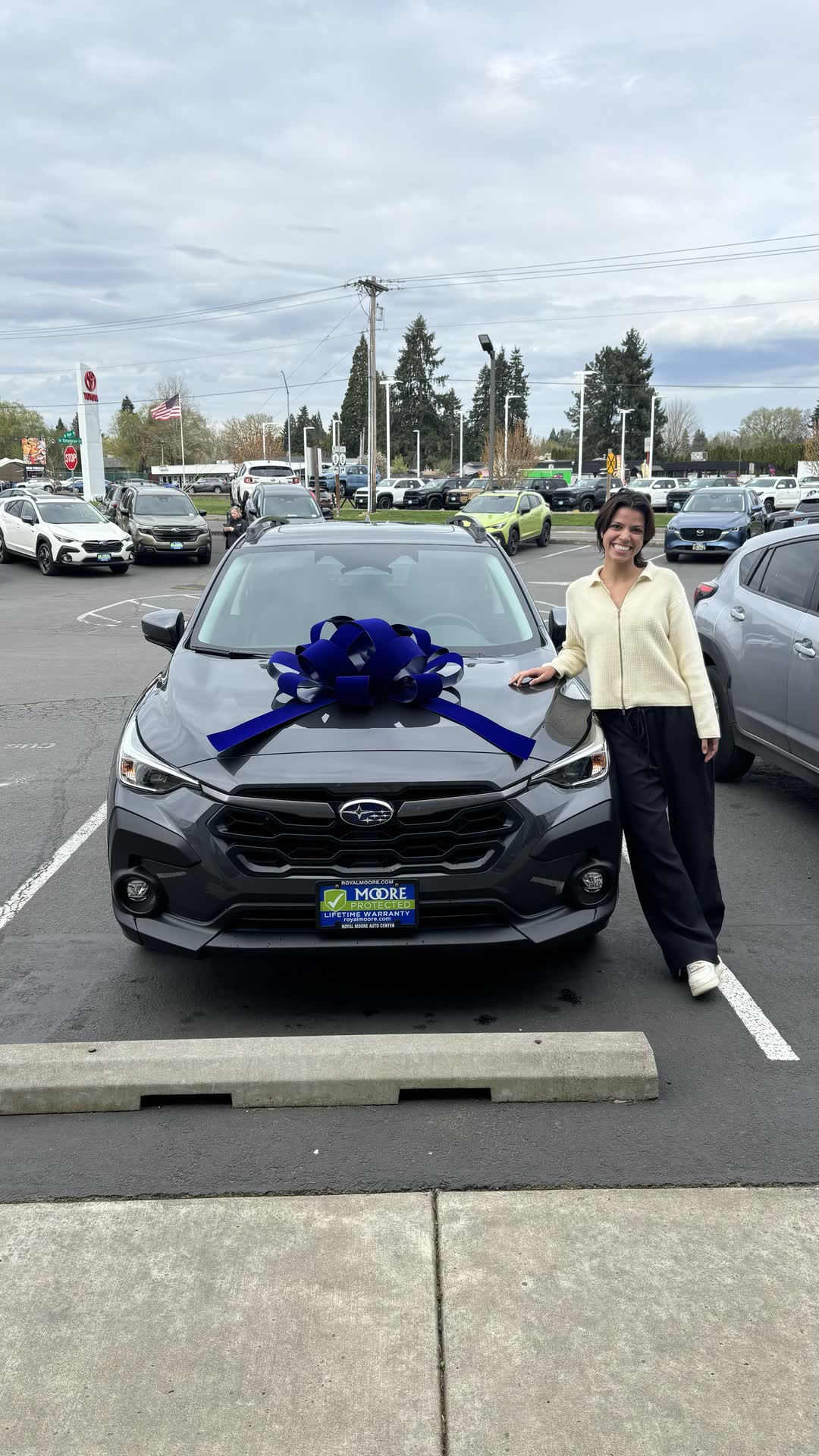 A customer beside the new Subaru she just leased at Royal Moore, blue bow on the hood